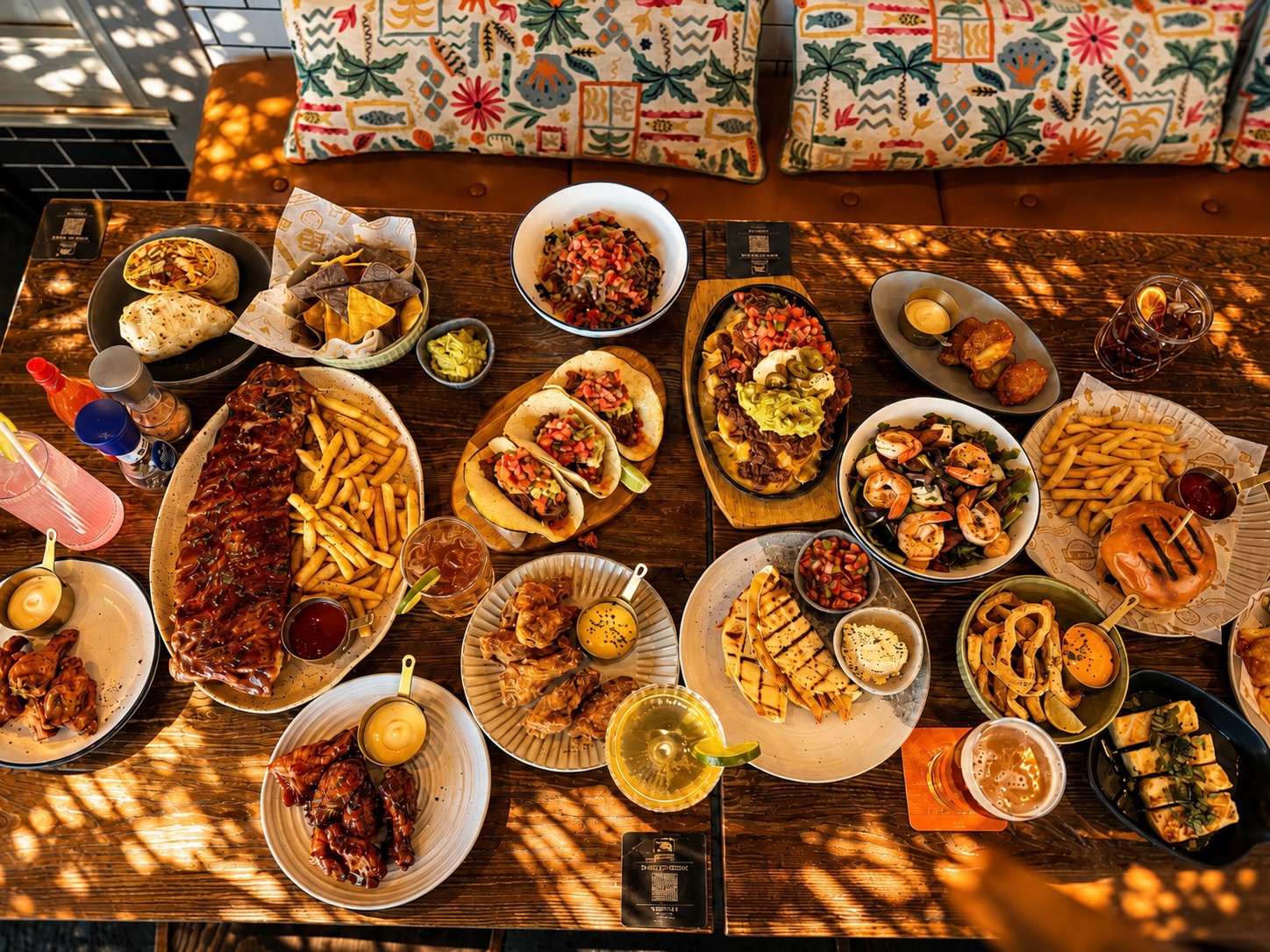 A table of tacos, ribs, burgers, nachos and drinks